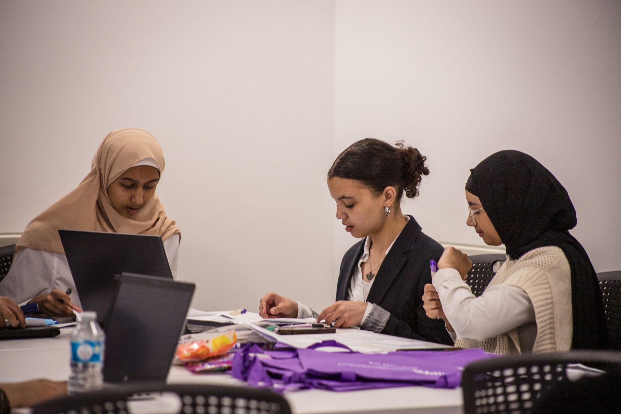 Three students sat around a table at a laptop