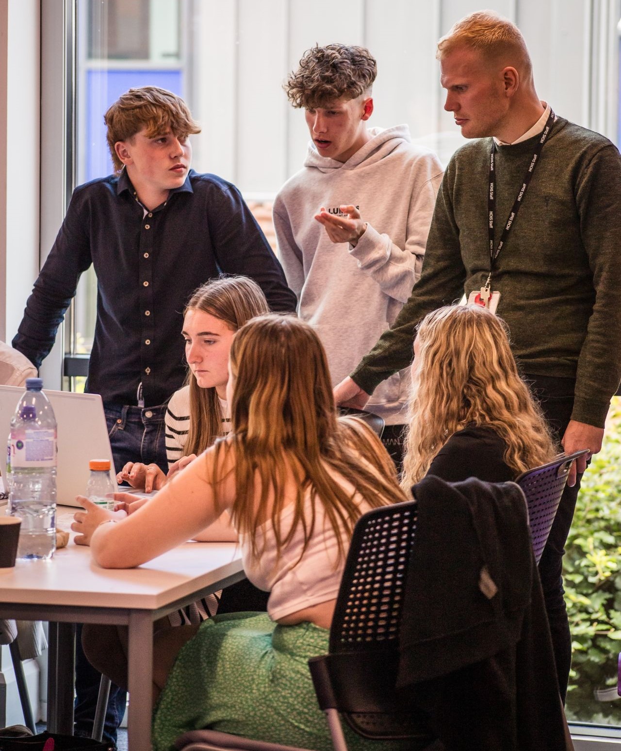 Group of students having a discussion sitting and standing around a laptop on a desk