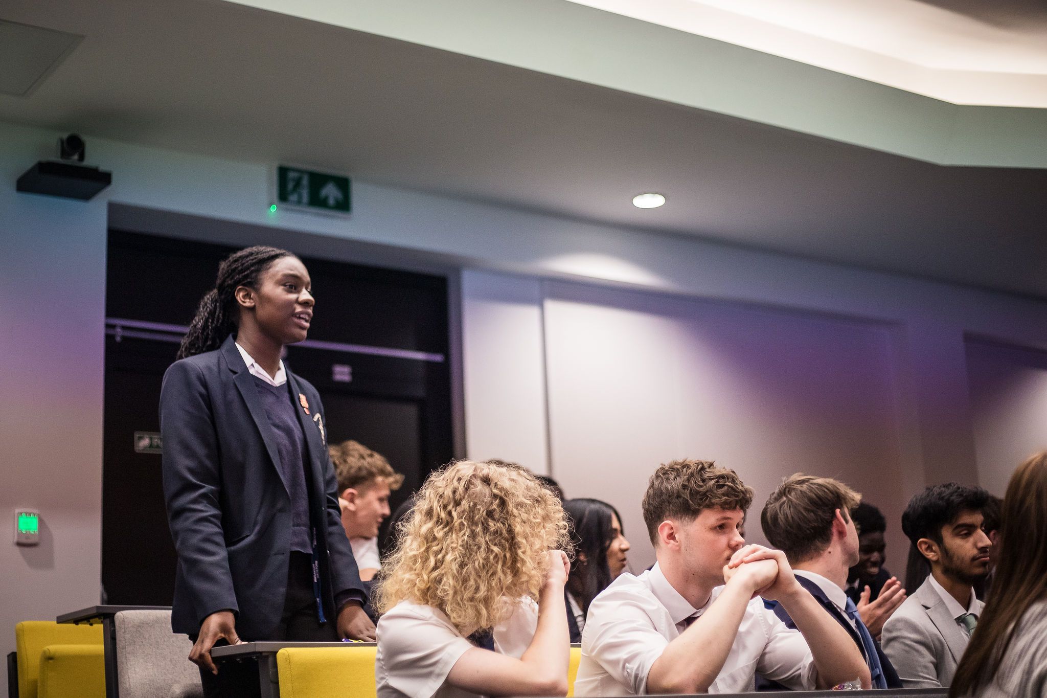 Students sat in a lecture hall, one student standing amongst them