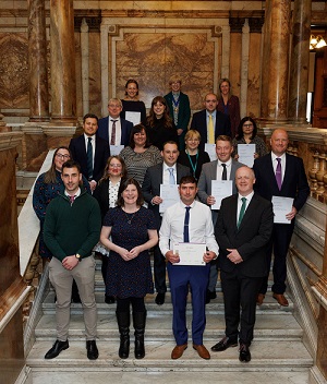 Group of graduates standing on steps showing their certificates