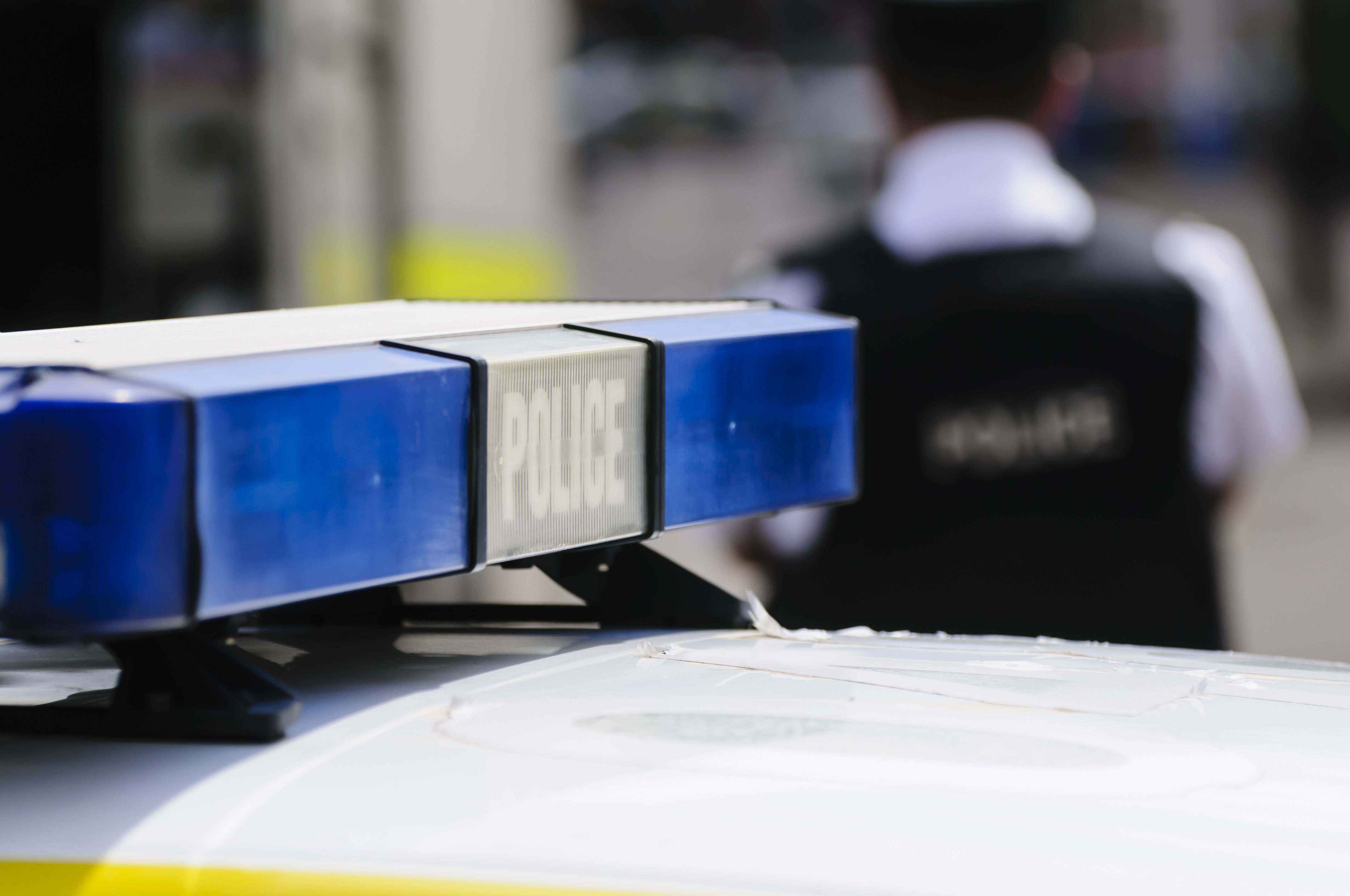 Focused Police siren on top of a Police car with the back of a uniformed officer out of focus 