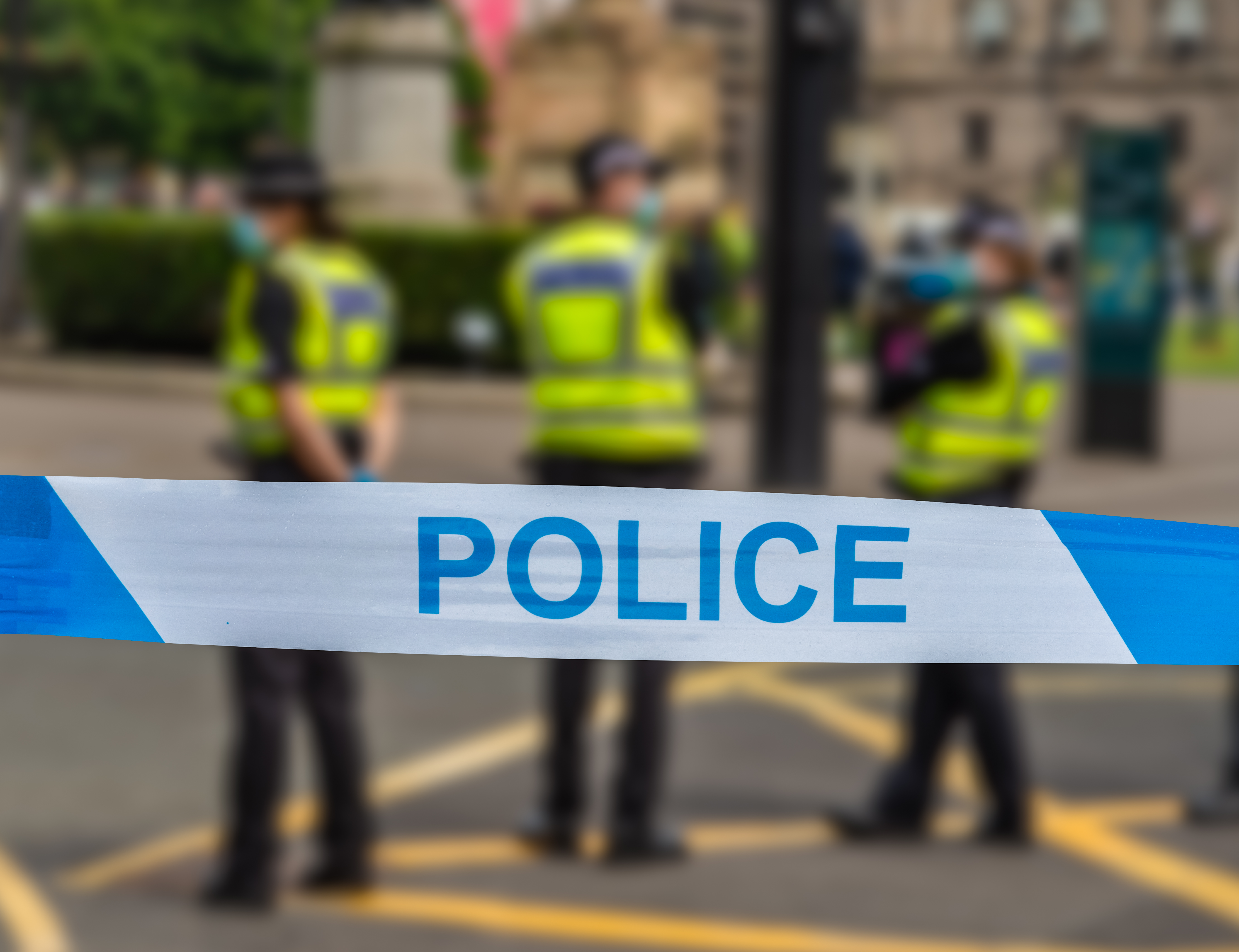 Three police officers standing on a street behind police tape.