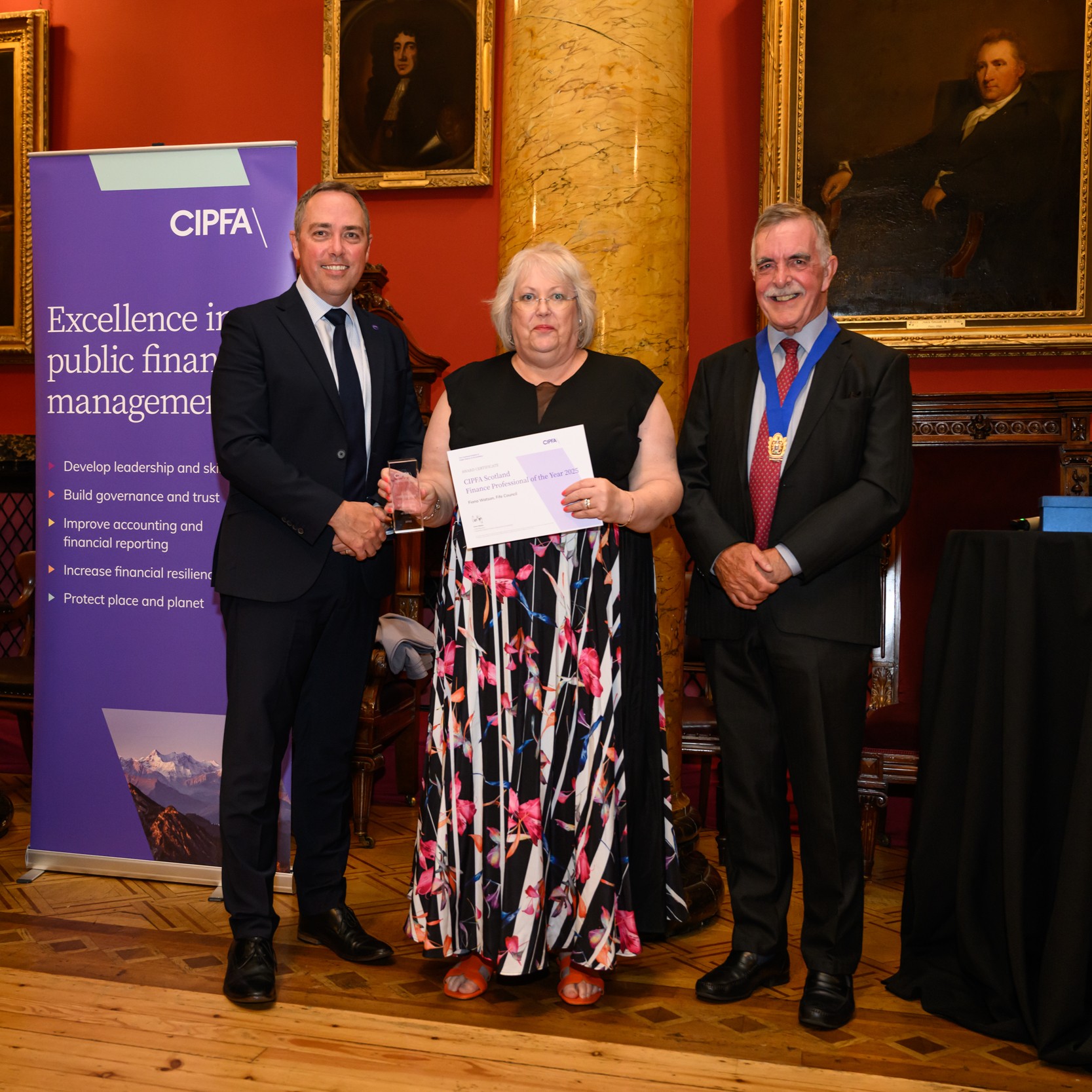 Smartly dressed woman holding a certificate standing with two smartly dressed men