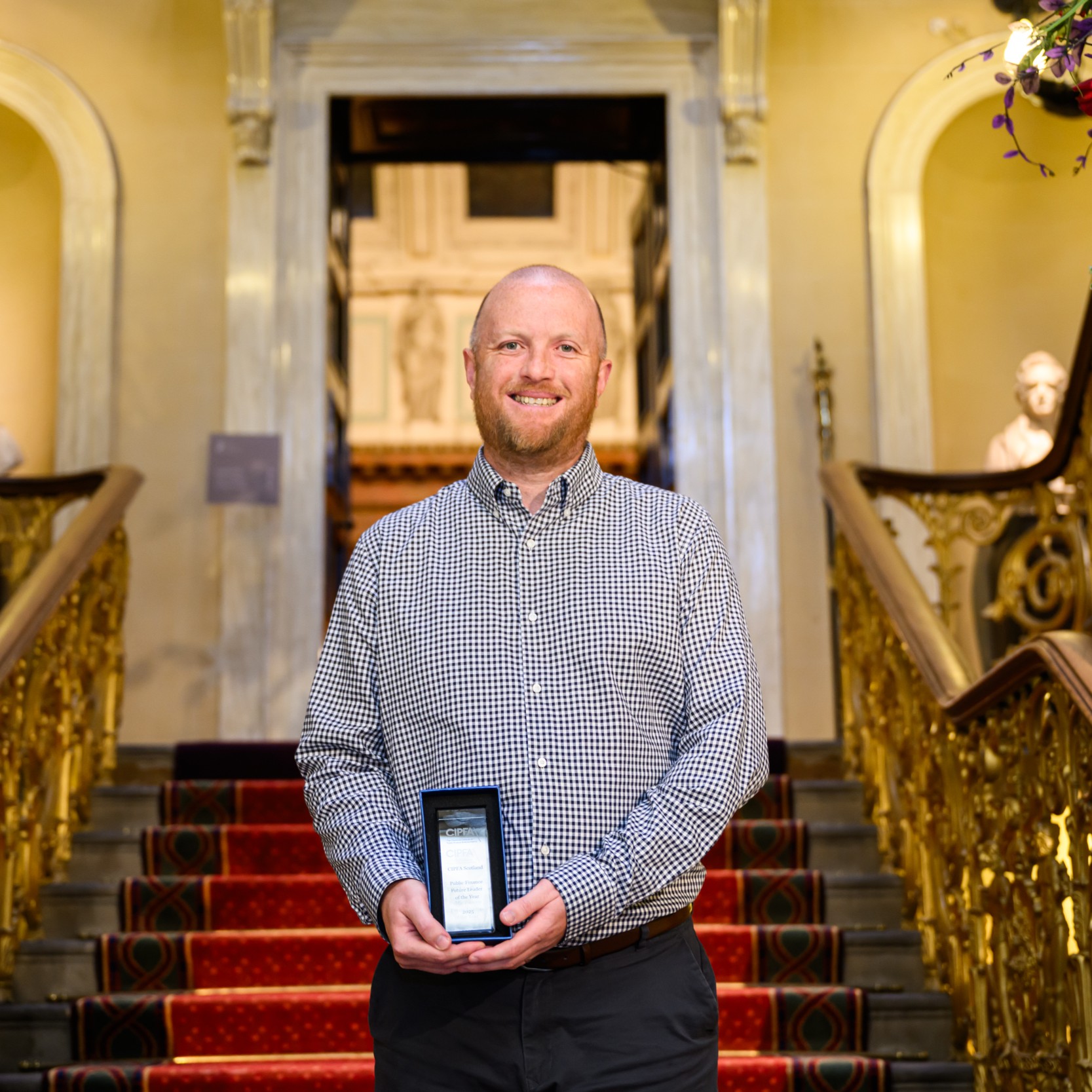 Man holding an award and the bottom of a grand staircase
